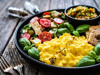Continental breakfast - scrambled eggs, bread and greek salad on wooden table
