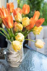 Yellow and orange tulips on the table in a vase. Summer on the balcony.