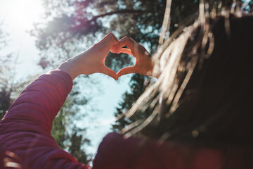 Hands in heart shape. One girl hands heart shape on against blurry forest background of summer or spring.Closeup