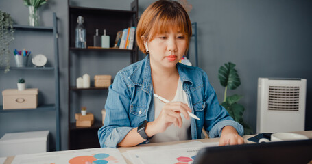 Asia businesswoman using tablet talk to colleagues about plan in video call while working from house at living room. Remotely at workplace, social distancing, quarantine for corona virus prevention.