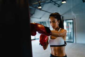 Young Asia lady kickboxing exercise workout punching bag tough female fighter practice boxing in gym fitness class. Sportswoman recreational activity, functional training, healthy lifestyle concept.