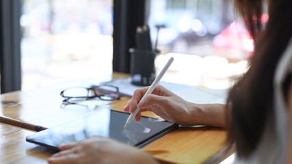Cropped shot of businesswoman holding stylus pen writing on digital tablet while sitting in cafe.