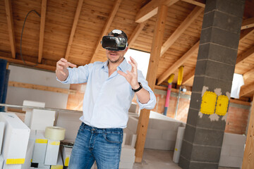 Man, builder with blue shirt looks at the conversion, extension of his loft with virtual 3d glasses and is on the construction site