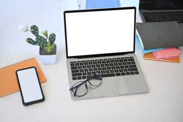 Mock up laptop computer, smart phone, cactus and notebook on white office desk.