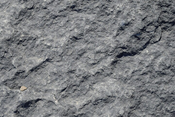 The texture of the rough surface of the rock is made of gray stone with cracks