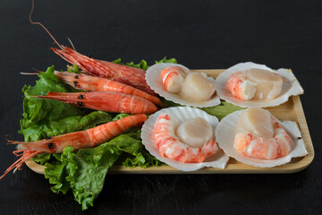 Natural raw scallop with boiled shrimp in the sink with a lettuce leaf in a wooden bowl on a dark background.