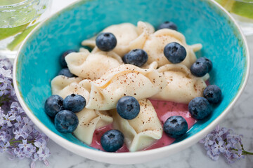 Closeup of curd dumplings or vareniki served with fresh bilberry in a turquoise bowl, selective focus