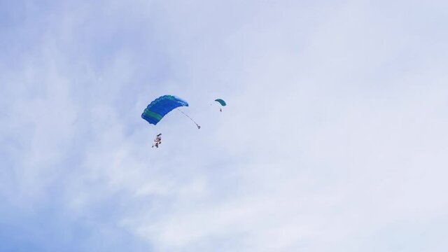 Parachutists Fly on a Paraglider Against Background of a Blue Sky with Clouds. Parachutists are paragliding. Tandem jumping. Skydiving in clear weather. Landing. 4K.