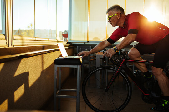 Man sitting on an exercise bike, exercising while watching video on laptop