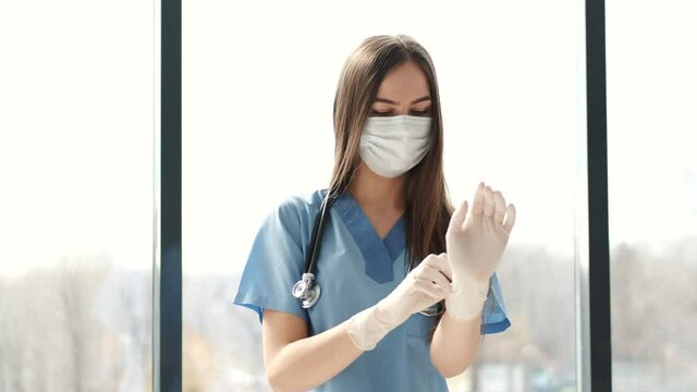 Young woman in a medical mask puts on protective gloves