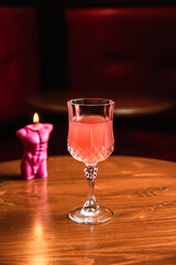 A pink cocktail in a beautiful crystal glass, a candle, on a wooden table, at the bar.