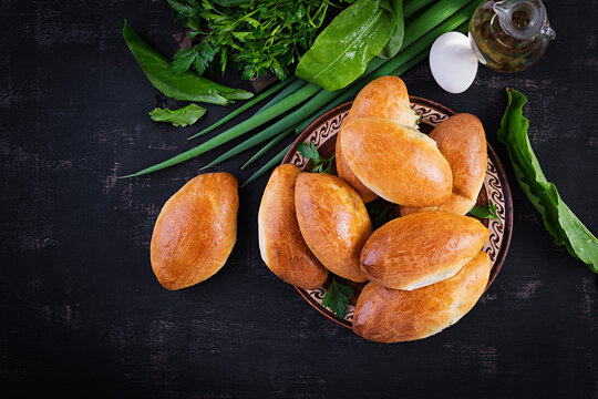 Traditional Ukrainian pies with eggs, green onion, sorrel on dark  background. Russian piroshki, homemade baked patties. Top view, above, copy space