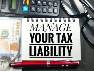 Business concept.Text MANAGE YOUR TAX LIABILITY with glasses,pen,calculator and banknote on black background.