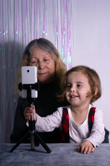 An elderly woman and a child are filming a video blog. Grandmother and granddaughter with a phone record video messages at home. Rest, relaxation, leisure concept.