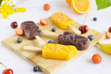 Group of homemade raspberry, cherries,strawberries, oranges, vanilla popsicles on a paddle board, frozen fruit juice, selective focus, white marble background