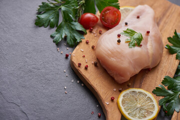 raw chicken fillet with garlic, pepper and rosemary on wooden on chopping board. fresh fillet. fresh chicken meat, chicken fillet with spices at black stone table. top view with copy space..