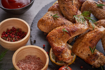 Roasted chicken wings in barbecue sauce with pepper seeds Rosemary, salt in a black stone plate on a gray stone table. top view with copy space. tasty snack for beer on a dark background. Flat lay.