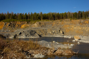 The beauty of a huge career in the Urals. Pine trees grow on quarries of a rocky quarry, mine workings, water at the bottom. Reddish rocks