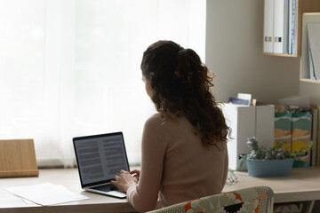 Back rear view young woman working on computer at home office, preparing electronic report...