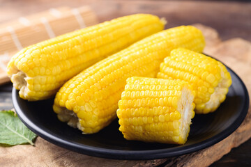Sweet corn cob on black plate with wooden background
