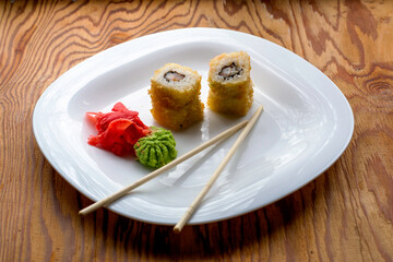baked sushi stacked on top of each other in two piles with eel wasabi ginger and chopsticks on a white plate