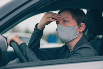 Worried woman with protective face mask having headache while waiting in the car