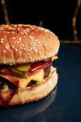 burger on a blue plate on a black background with a golden twig overhead side view
