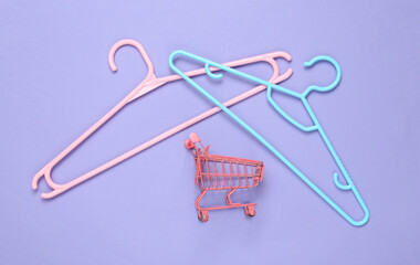 Fototapeta premium Plastic hanger with mini shopping trolley on purple background. Fashion layout. Flat lay. Top view