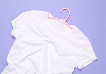 Hanger with white t-shirt on purple background. Top view