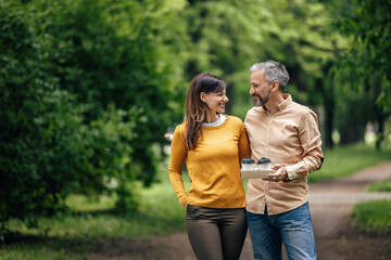 Adult man, holding cups of coffee, looking at his wife.