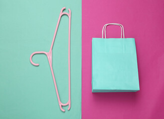 Hanger and paper shopping package on pink blue background. Top view. Minimalism