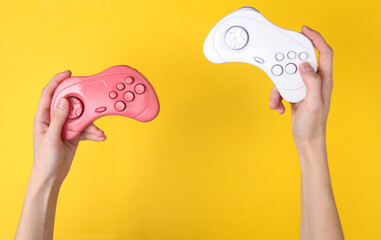 Female hands hold retro gempads on yellow background. Gaming concept