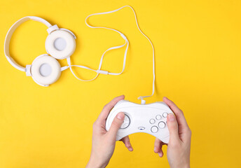 Female hands hold retro gempads on yellow background with headphones. Gaming concept