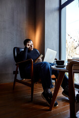 A young girl with glasses, with short hair is sitting in a cafe and working on a laptop. The girl looks at her laptop and makes notes in a notebook. The concept of distance learning