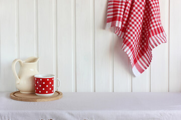 white pitcher, red towel and a polka-dot mug on the table.