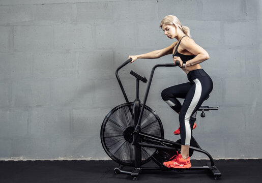 Woman doing intense cardio training on exercise bike. Fitness female using air bike for cardio workout at gym
