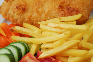 Traditional english dish with battered white cod, french fries and fresh vegetable served on a white plate. Close up