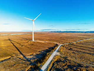 White wind turbine with propellers in a field. Aerial drone view, Clean blue sky, Sunrise time. Renewable eco friendly source of energy. Green energy concept. Technology to produce power © mark_gusev