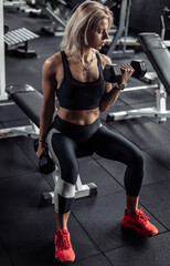 Fototapeta na wymiar Athletic woman in sportswear trains biceps with heavy dumbbells in her hands at gym. Healthy lifestyle, fitness and bodybuilding concept.
