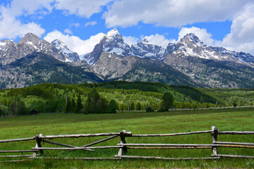the magnificent peaks of the grand teton mountain range with a split rail fence in a pasture on a...