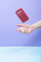 Hand and Levitating pink calculator on colored background. Minimalistic still life. Creative layout. Concept art