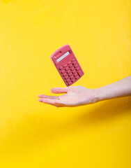 Hand and Levitating pink calculator on yellow background. Minimalistic still life. Concept art