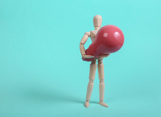 Wooden puppet holding pink light bulb on blue background