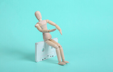 Wooden puppet with white audio cassette on blue background