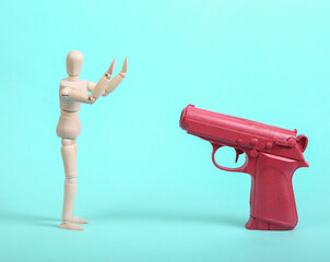 Pistol aimed at frightened puppet with raised hands on blue background