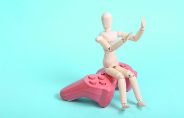 Wooden puppet with pink gamepad on blue background
