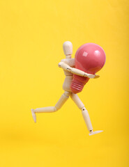 Wooden puppet holding pink light bulb on yellow background
