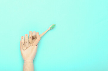 Wooden hand holding Eco-friendly bamboo toothbrush on blue background.