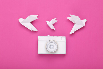 White painted camera and origami doves on a pink background. Minimalism