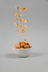 flying food concept - dried pineapple pouring into a bowl against gray background
